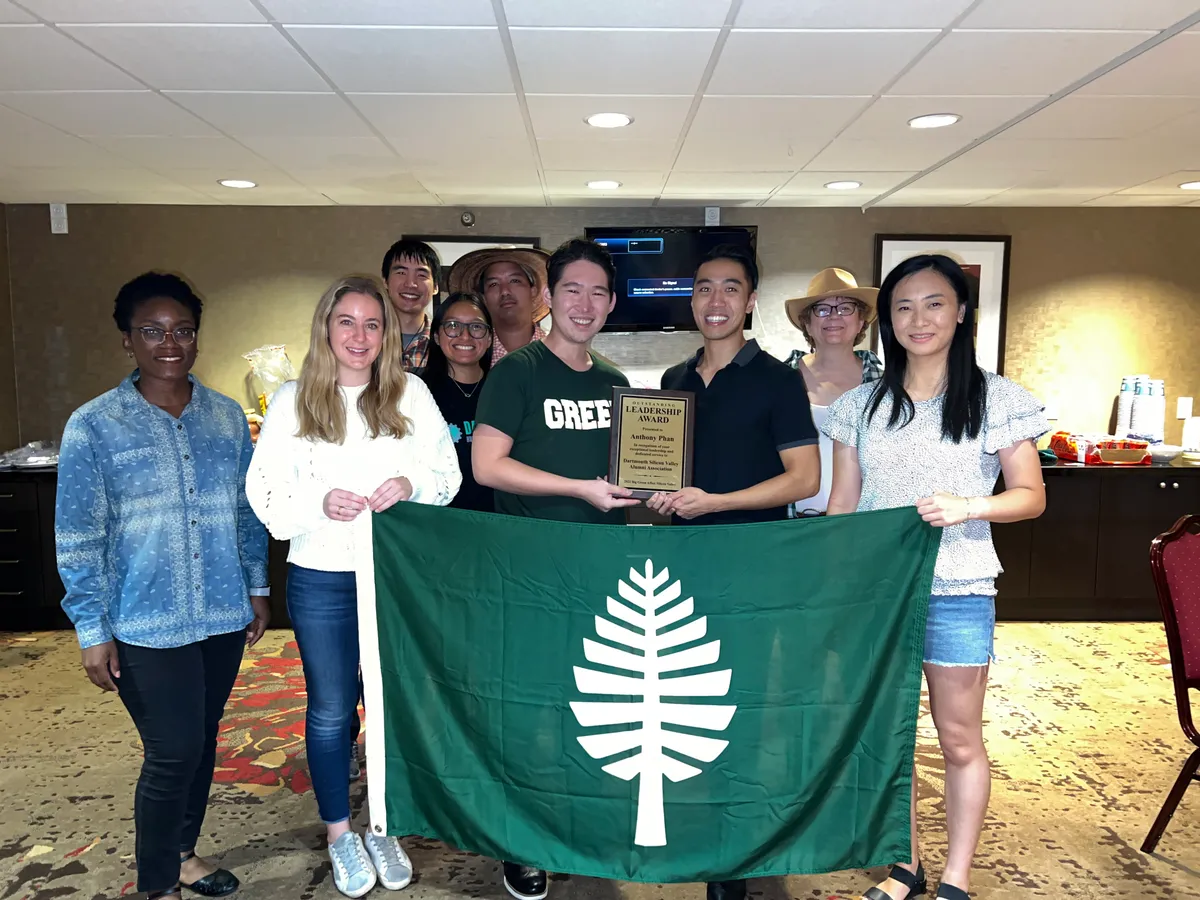 A group behind a green Dartmouth pine flag, two of them holding an Outstanding Leadership Award plaque.